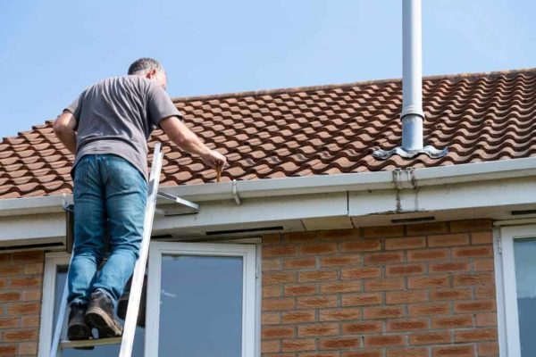 Senior man cleaning gutters on a suburban English house.